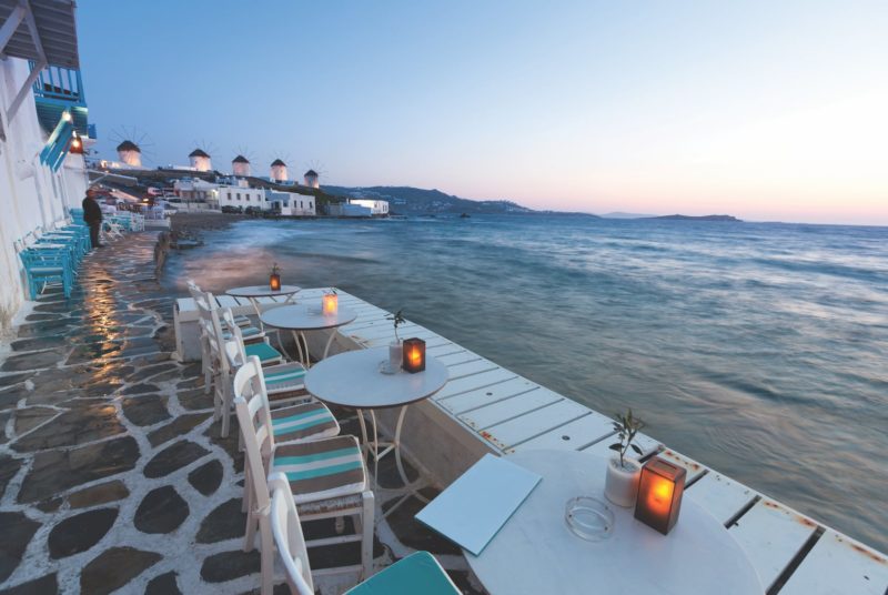 Little tables and chairs overlooking the sea in Mykonos. Traditional windmills at the back.