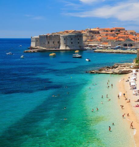 Overview of a beautiful beach in Dubrovnik, a Medieval castle and traditional houses.