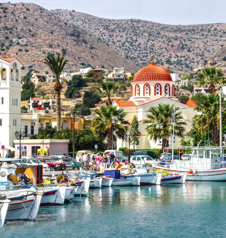 Greek church and fish boats in a little port. Imposing mountains at the back.