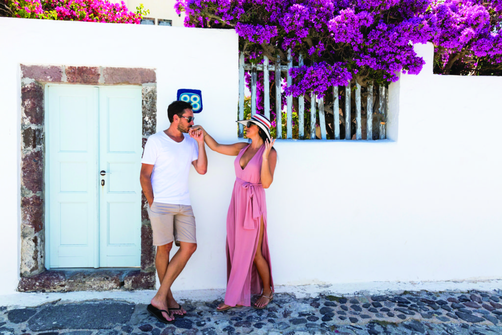 Man and woman by a white door of a luxury accommodation in a Greek island.